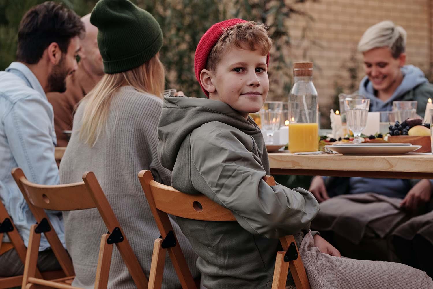 Eine Gruppe Menschen sitzt am einen Holztisch unter freien Himmel.