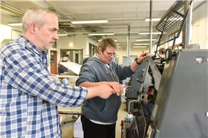 Frau mit Behinderung arbeitet zusammen mit Betreuer in Werkstatt f. Menschen mit Behinderung.