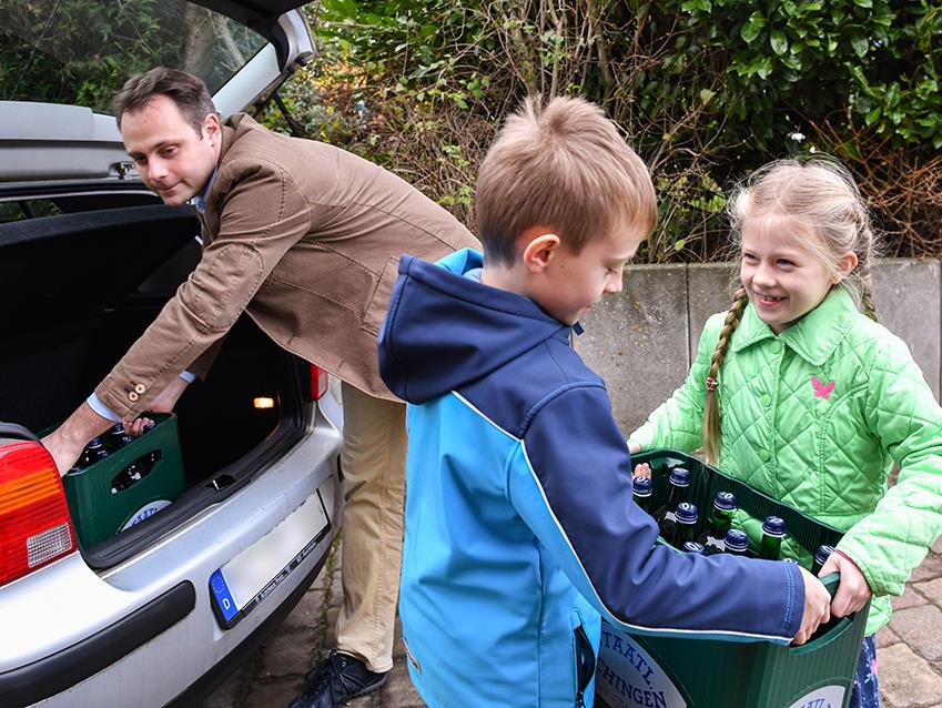 Vater mit zwei Kindern beim Auto ausladen