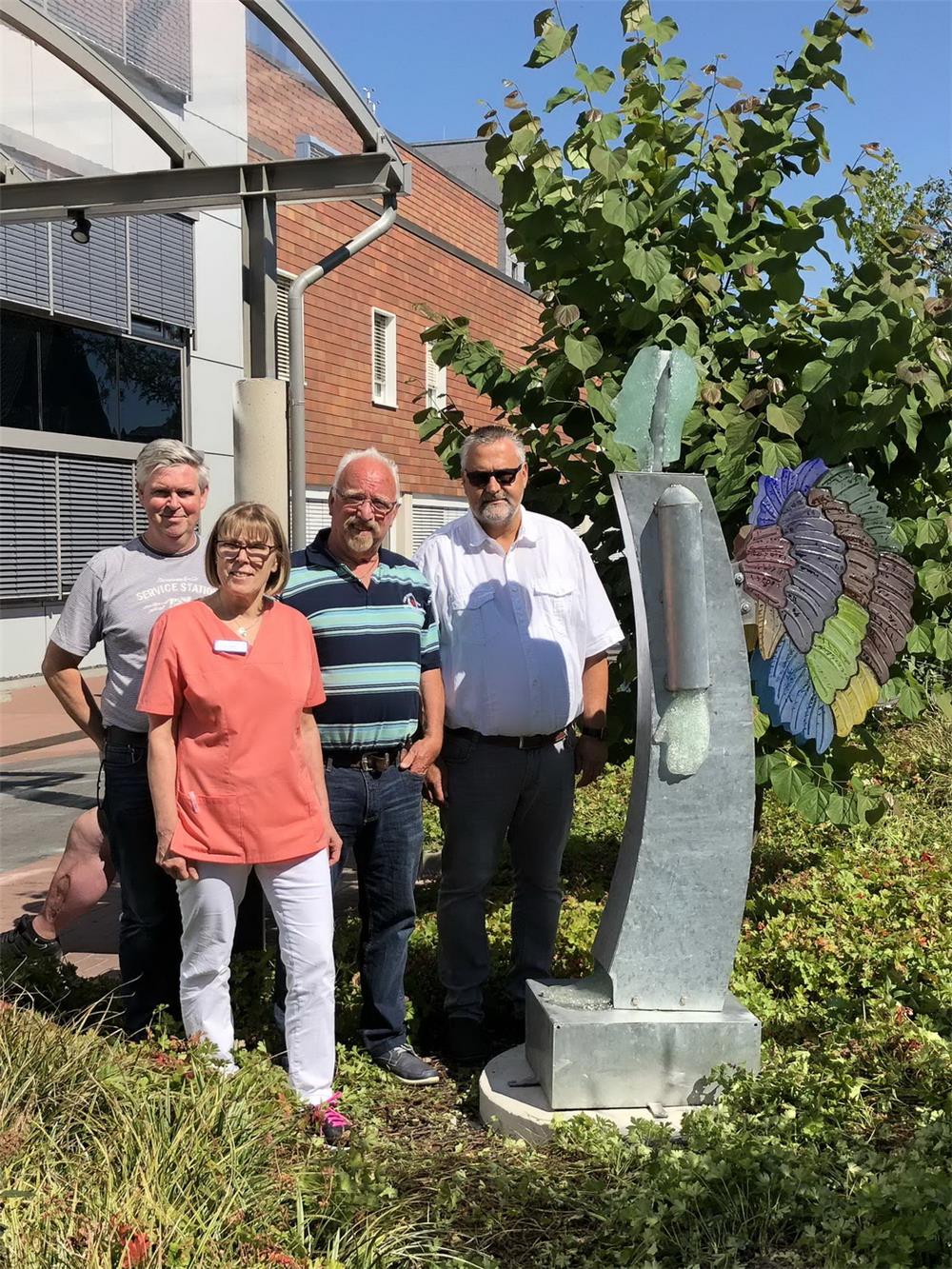 Vier Personen stehen hinter einen Glasskulptur, die einen Engel darstellt.