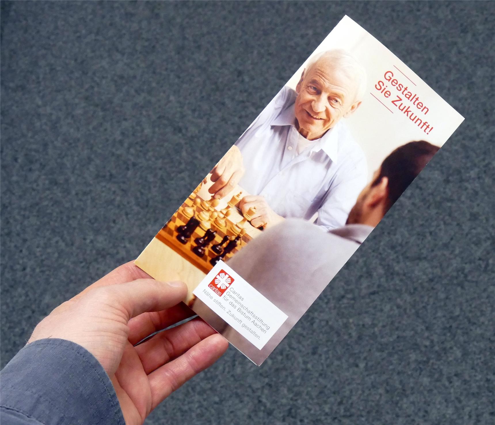 Hand hält Flyer der Caritas-Gemeinschaftsstiftung für das Bistum Aachen
