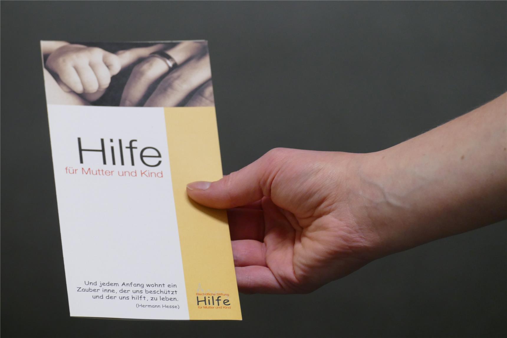 Frauenhand hält Flyer der Stiftung Mutter und Kind