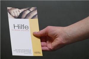 Frauenhand hält Flyer der Stiftung Mutter und Kind