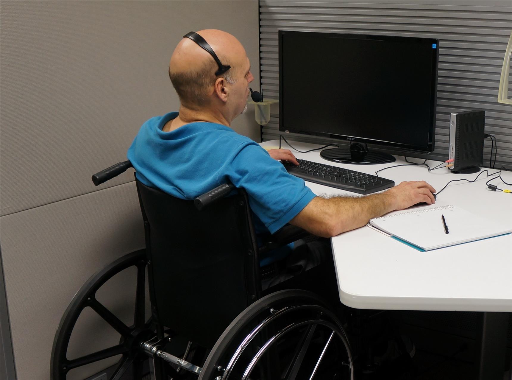 Mann im Rollstuhl mit Headset am Arbeitsplatz