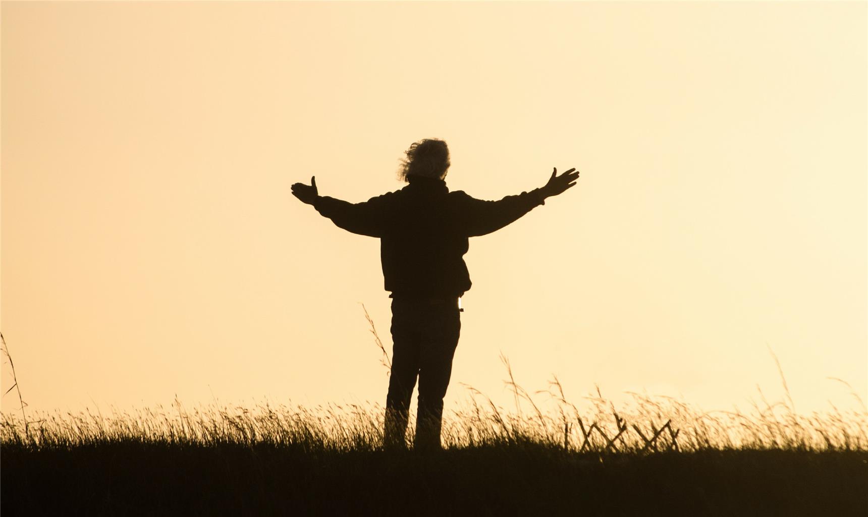 Mensch von hinten im Gegenlicht mit ausgebreiteten Armen