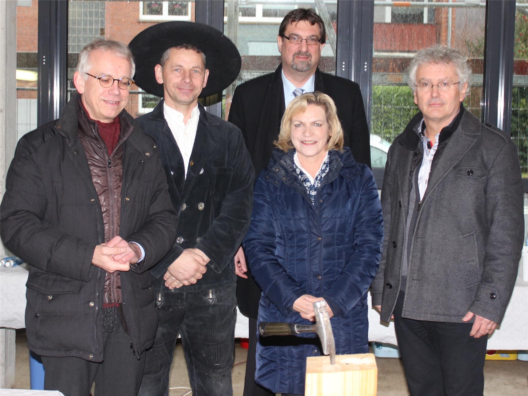 Fünf Erwachsene stehen beim Richtfest um einen Holzbalken, auf dem ein Hammer liegt.