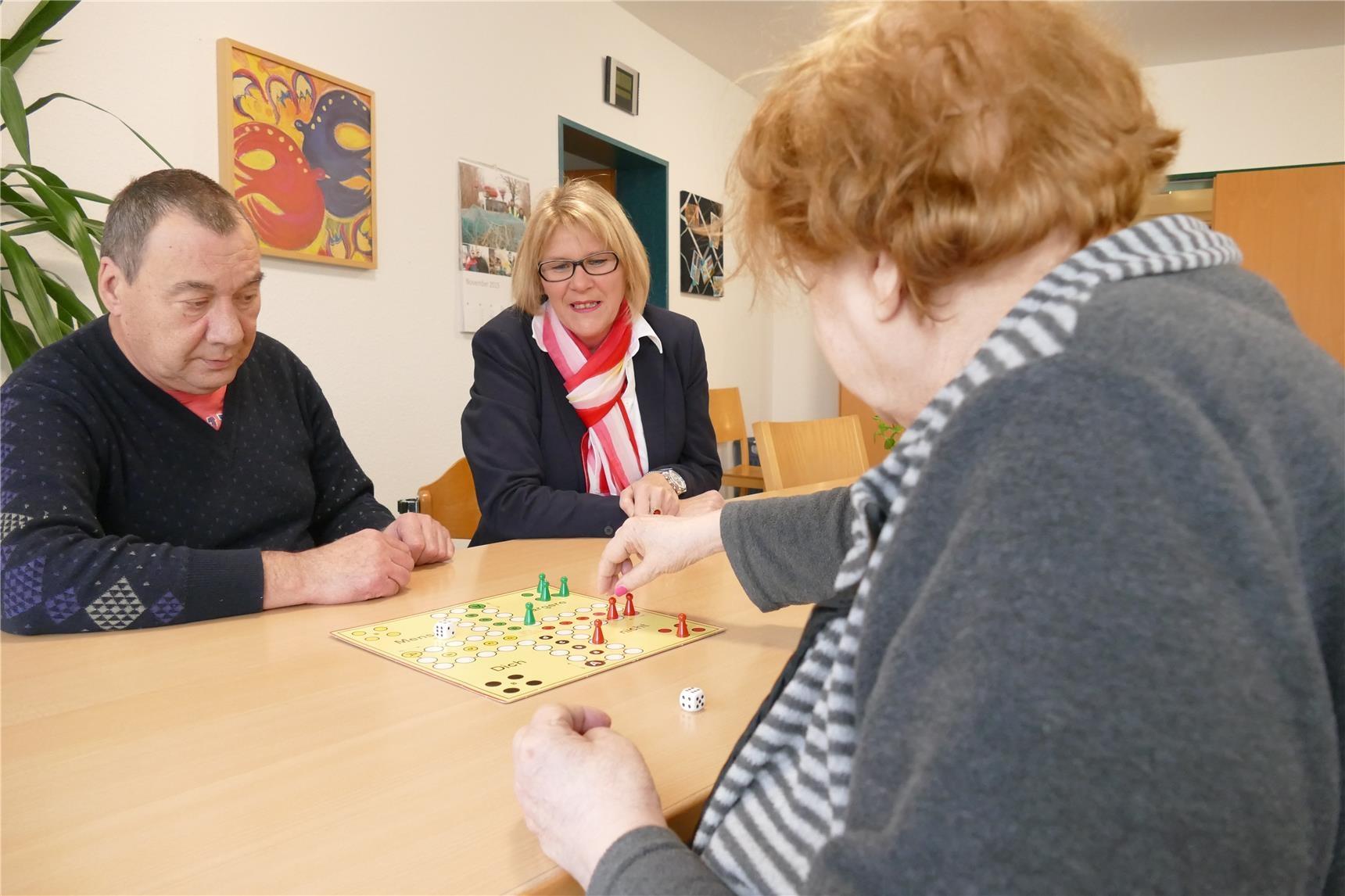 Frau schaut zwei Erwachsenen beim Brettspiel zu