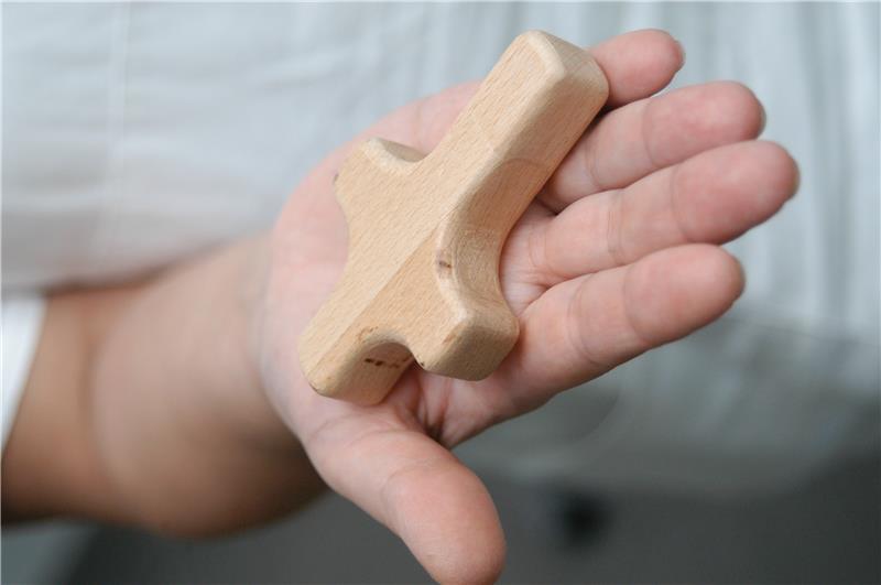 Hand mit einem weichen Holzkreuz mit abgerundeten Kanten