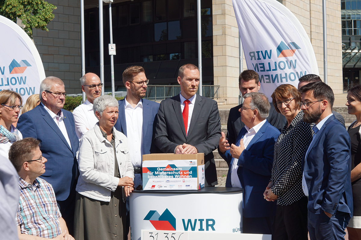 Vetreter des Aktionsbündnisses 'Wir wollen wohnen!', Abgeordnete des Landtags und Staatssekretär Dr. Jan Heinisch stehen an einem Stand des Bündnisses vor dem NRW-Landtag
