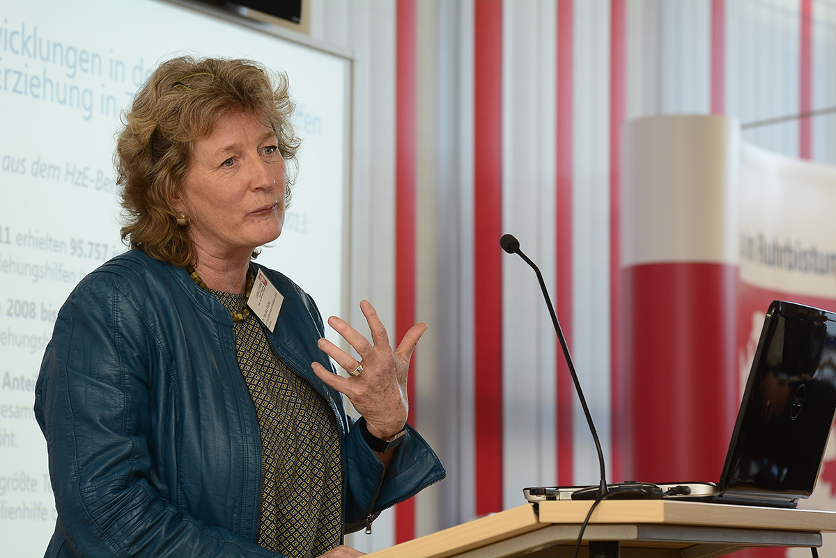 Dr. Monika Weber steht bei der Fachtagung 'Ambulante Hilfen zur Erziehung zwischen Wirksamkeit und Kostendruck' der Caritas in NRW vor einem Pult und hält eine Rede