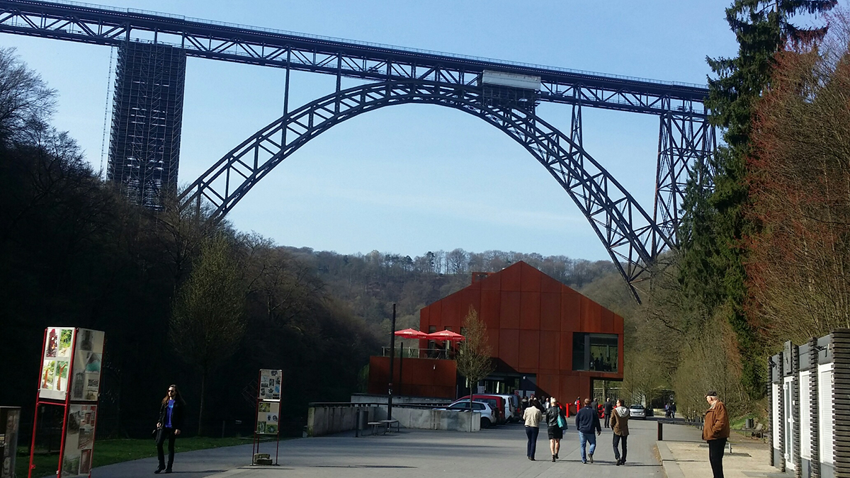 Das Haus Müngsten und die Müngstener Brücke in Solingen in der Frontansicht. Im Vordergrund ist ein Fußweg mit einigen Menschen zu sehen.