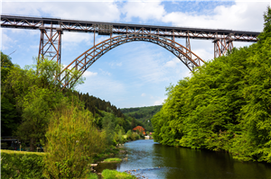 Die Müngstener Brücke (stählernde Bogen-/Eisenbahnbrücke) in Solingen, unter der die Wupper durchfließt. Die Uferseiten sind dicht bewachsen, im Hintergrund ist das Restaurant
