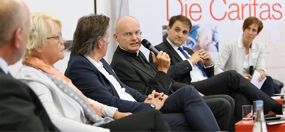 Eine Teilnehmerin, vier Teilnehmer und eine Moderatorin, die bei der Podiumsdiskussion beim Ruhrgebietstag auf der Bühne zusammen sitzen. Ein Teilnehmer hält ein Mikrofon in der Hand und redet.