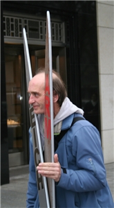 Ein Mann während einer Aktion von Caritas/Nationalen Armutskonferenz auf der Königsallee in D'dorf. Er hält seinen Kopf zwischen eine riesige Holzschere mit der Beschriftung Arm und Reich.