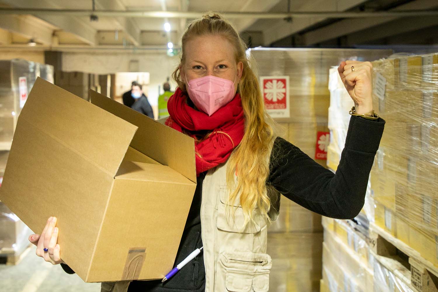 Junge Frau mit langen blonden Haaren trägt einen Karton und spannt den Bizeps an.