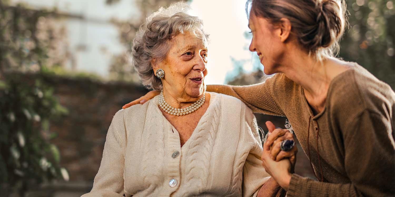 Eine ältere Dame im Rollstuhl wird von einer jungen Frau umarmt.