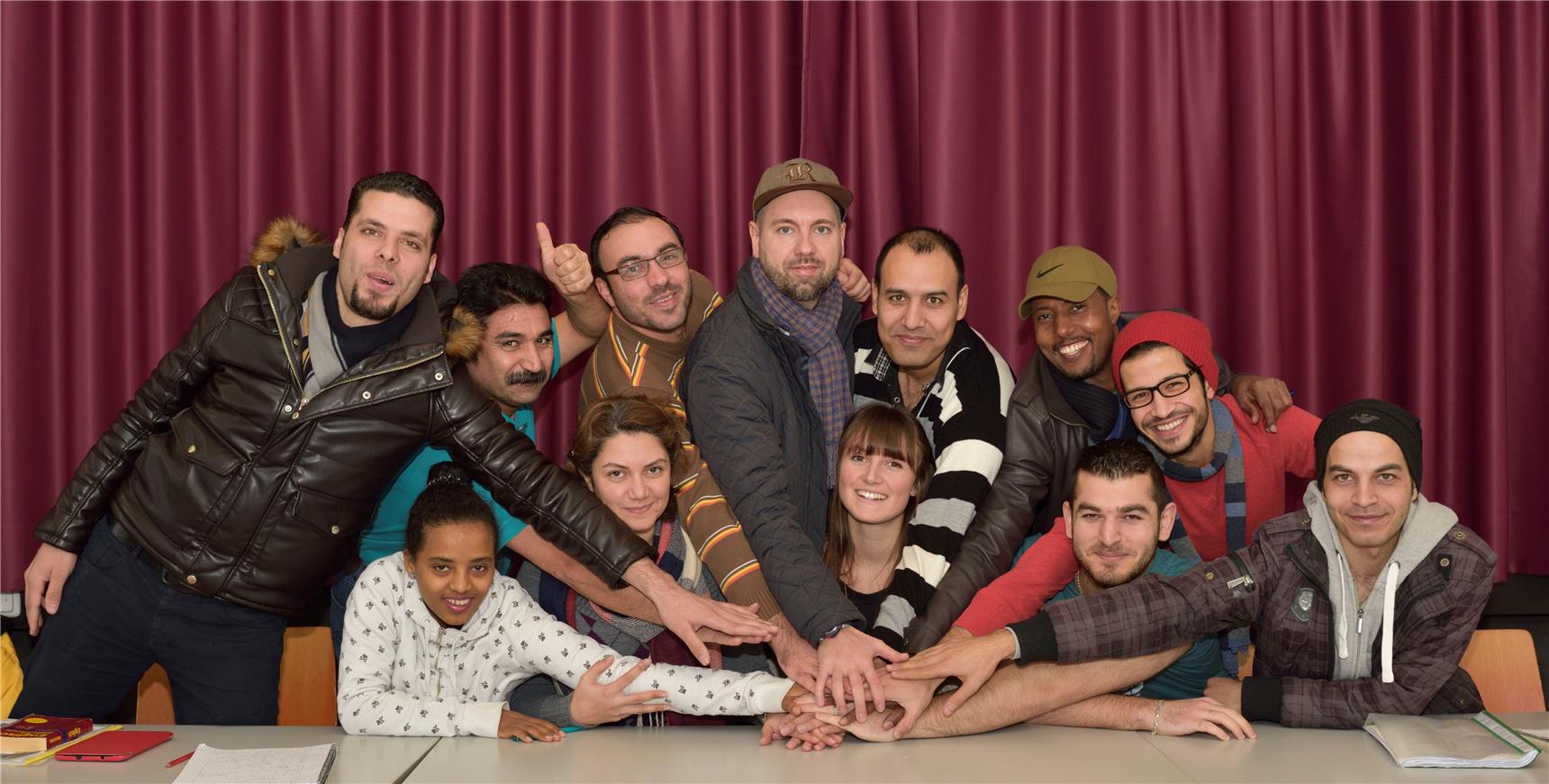 Auf dem Bild sind viele junge Studenten und Studentinnen und Flüchtlinge zu sehen, die zusammen fröhlich lachen