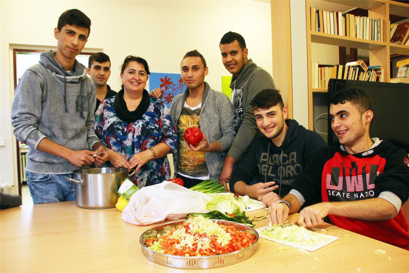 Sechs junge Männer und eine Frau stehen vor leckeren Zutaten, welche auf einem Tisch vor ihnen liegen.